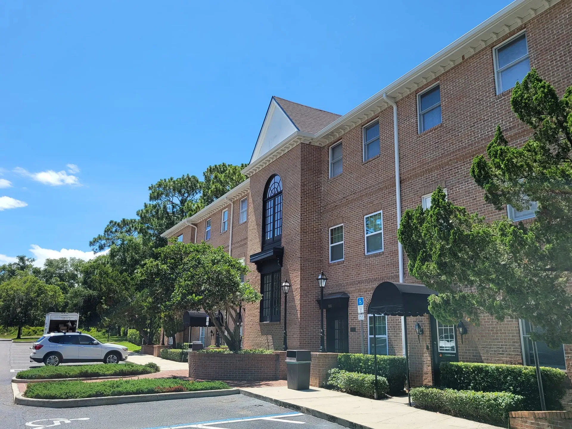 Three story brick office building white gutters black awnings parking lot sanfor